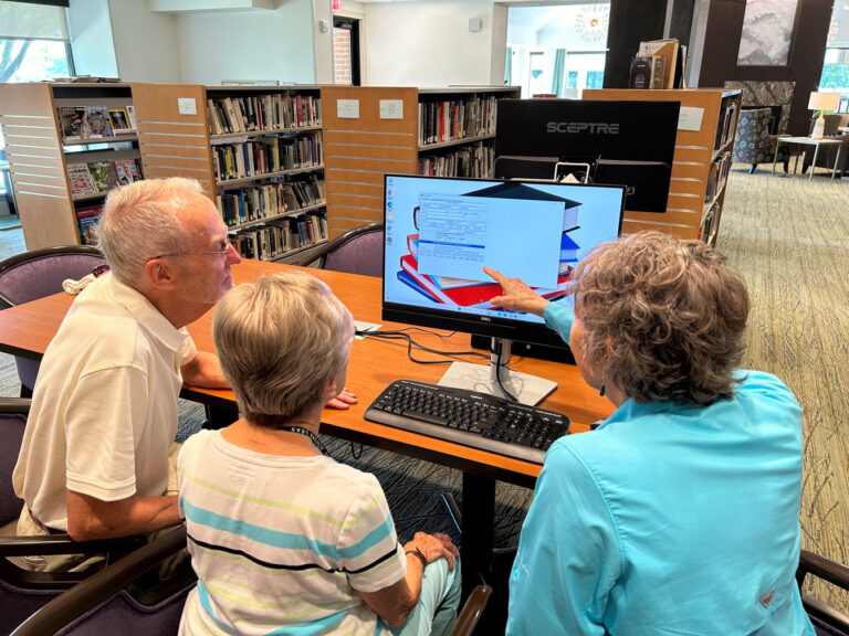 3 people seated in front of computer with one of them pointing at something on the screen